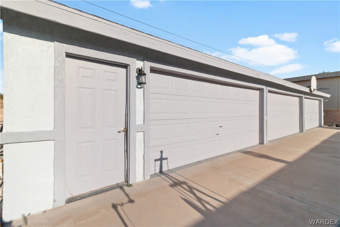 784 Pegasus Ranch Road Bullhead City, AZ 86429 - Photo 54 of 100 Multiple garage bays with roll-up doors, stucco exterior, and an exterior door with a wall-mounted light fixture