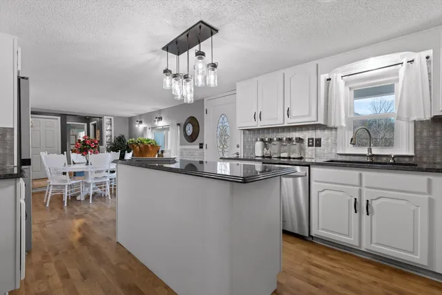 a kitchen with stainless steel appliances granite countertop a stove top oven a sink a dining table and chairs with wooden floor