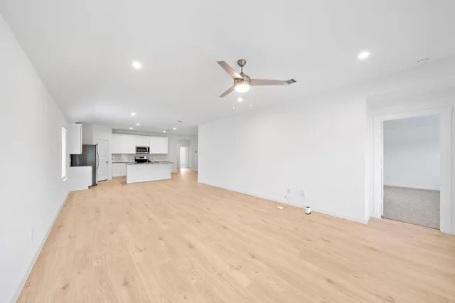 a large kitchen with kitchen island a stove a sink a refrigerator and white cabinets with wooden floor