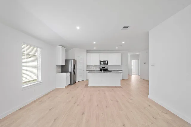 a large white kitchen with kitchen island a sink wooden floor and view living room