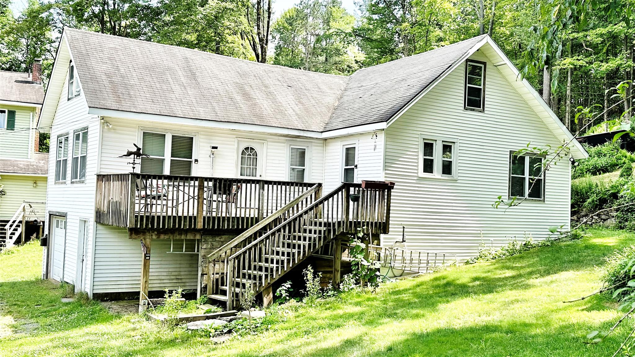 Rear view of house with stairway, a wooden deck, a lawn, and a shingled roof