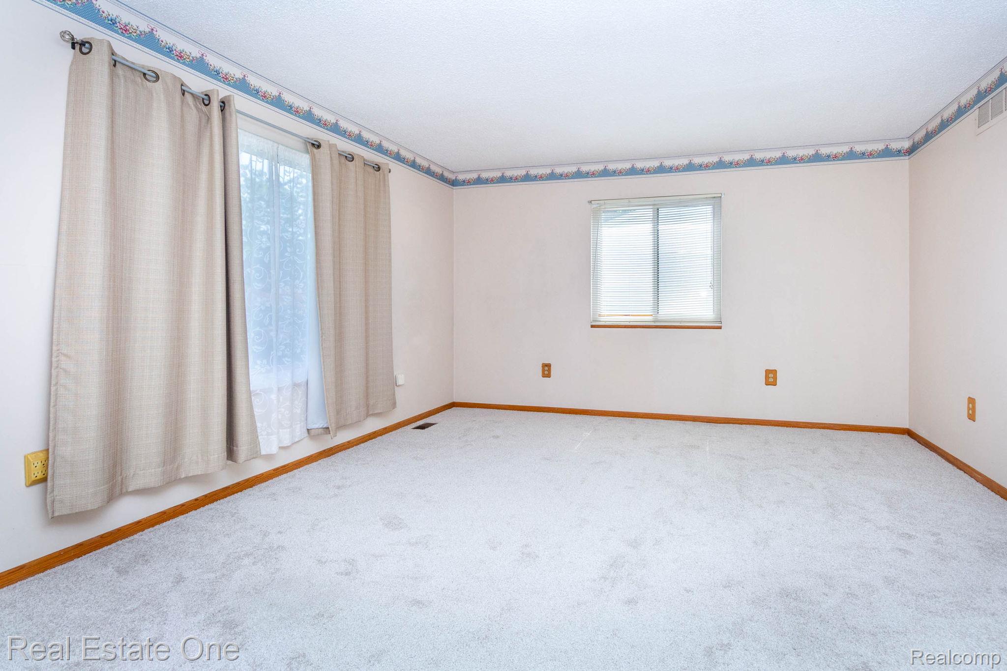 13912 Clinton River Road Sterling Heights, MI 48313 - Photo 6 of 43 Carpeted room with multiple windows, featuring a decorative wallpaper border and wood-finish baseboards