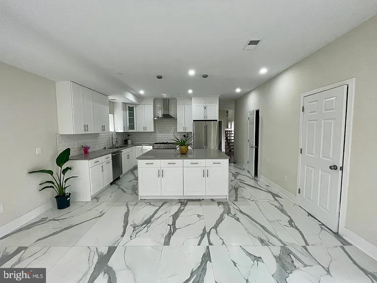 8618 Jones Mill Road Chevy Chase, MD 20815 - Photo 18 of 59 a large white kitchen with kitchen island a stove a sink a refrigerator and white cabinets with wooden floor