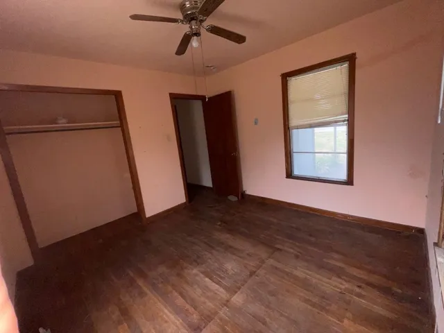 an empty room with wooden floor closet and windows