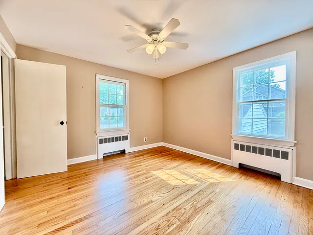 an empty room with wooden floor fan and windows
