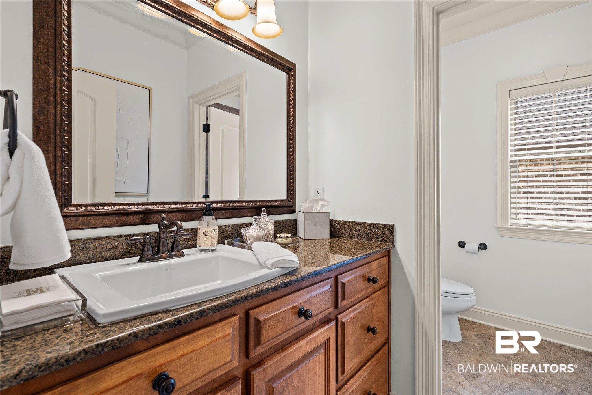 3459 Rue Royal Mobile, AL 36693 - Photo 21 of 31 Bathroom vanity with an integrated sink, granite countertop, wood cabinetry with black hardware, and an ornate framed mirror