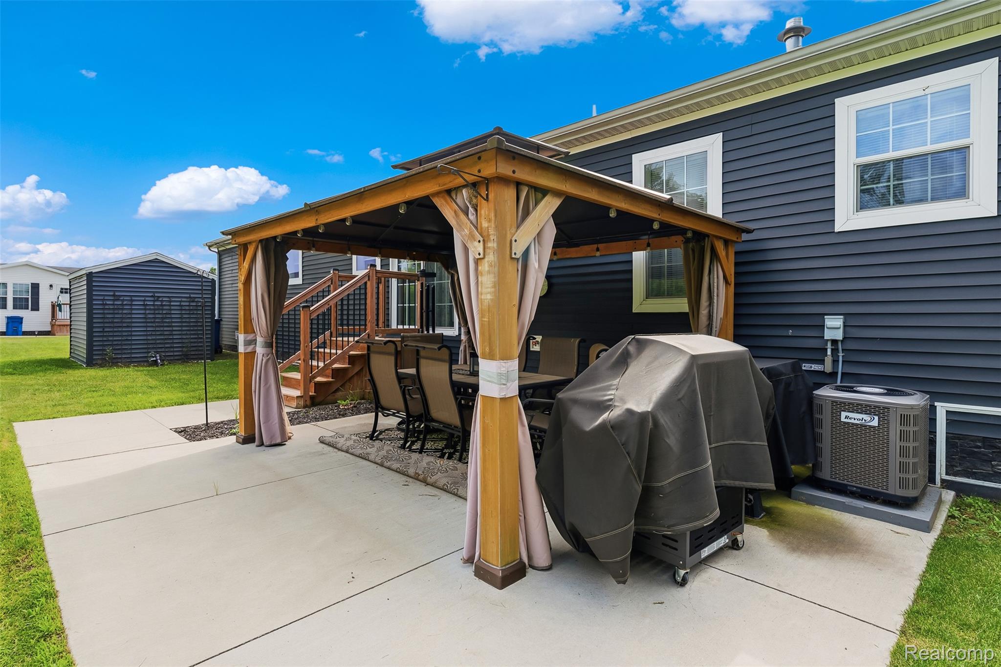 6450 Prince Boulevard Fenton, MI 48430 - Photo 28 of 31 Outdoor patio with a permanent wooden gazebo, concrete surface, and direct access to the rear deck via wood stairs with black railings
