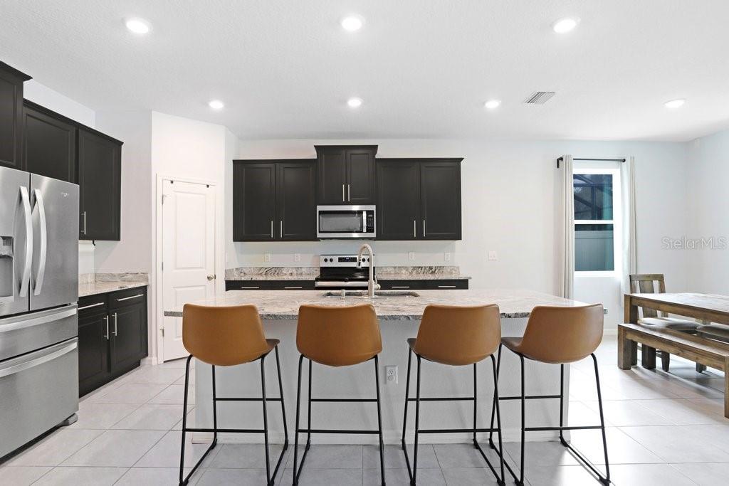 16619 Goose Ribbon Place Wimauma, FL 33598 - Photo 7 of 38 a kitchen with stainless steel appliances granite countertop a stove a sink a microwave a island with a dining table and chairs