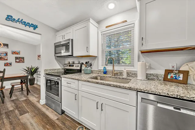 a kitchen with granite countertop stainless steel appliances white cabinets and a window