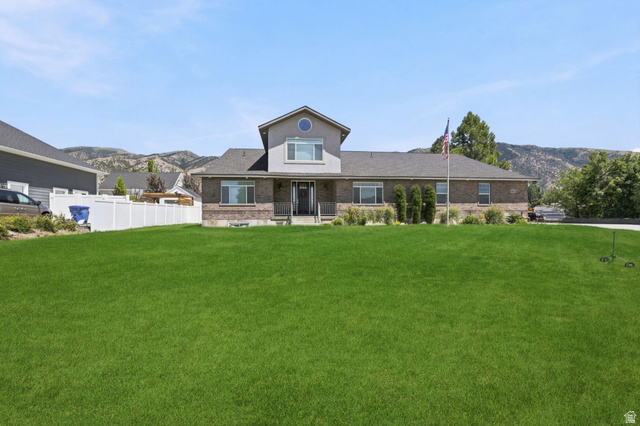 580 North 300 East Logan, UT 84321 - Photo 18 of 74 Expansive front lawn with a brick and siding exterior, a white picket fence, and a mountain backdrop