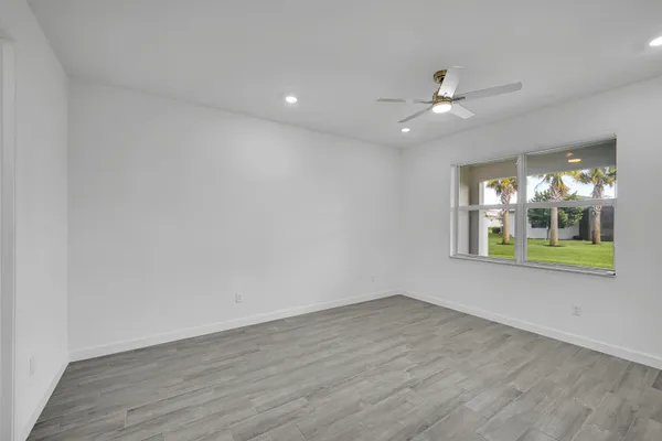 an empty room with wooden floor fan and windows