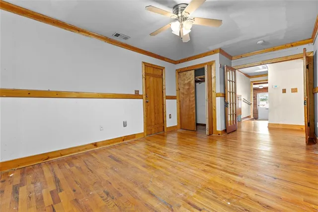 a view of an empty room with wooden floor and a ceiling fan