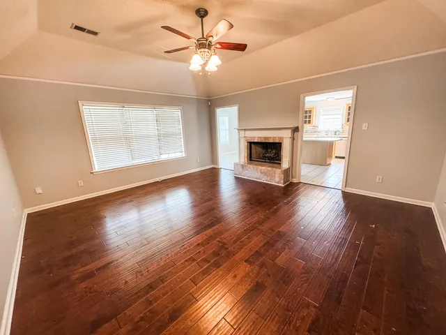 an empty room with wooden floor chandelier fan and windows
