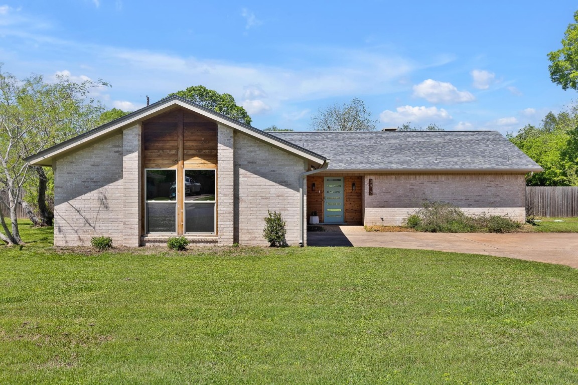 Mid-century inspired home featuring roof with shingles, fence and brick exterior.