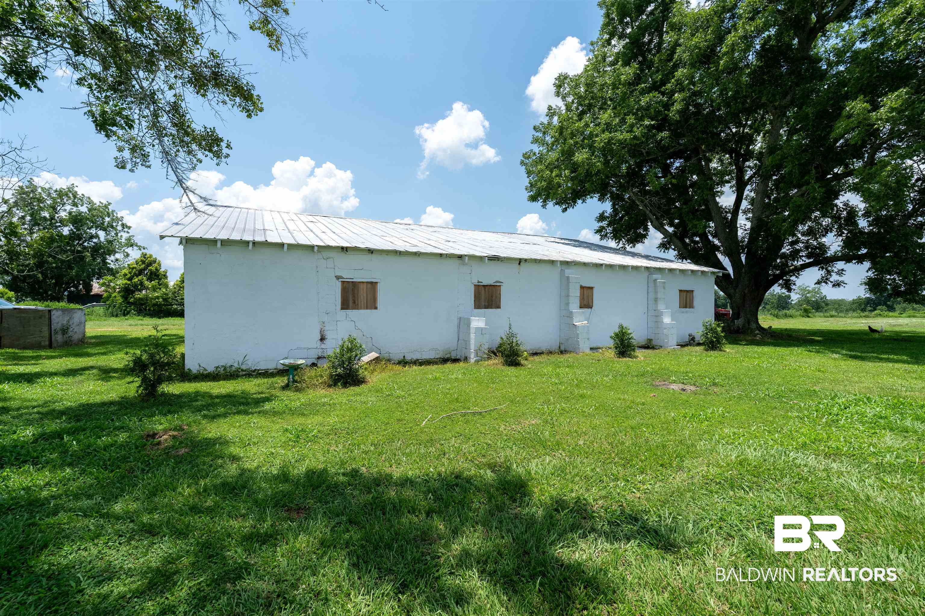 15575 Mikkelsen Road Summerdale, AL 36580 - Photo 30 of 68 White-painted exterior structure with a metal roof and multiple small window openings, situated within a spacious grassy area with mature trees