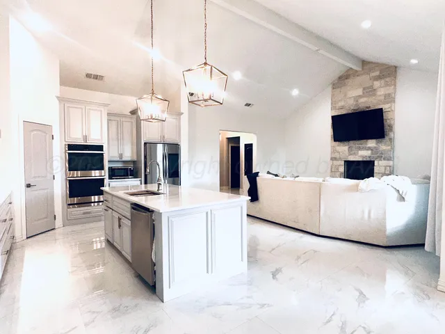 a living room with stainless steel appliances furniture a flat screen tv and a kitchen view