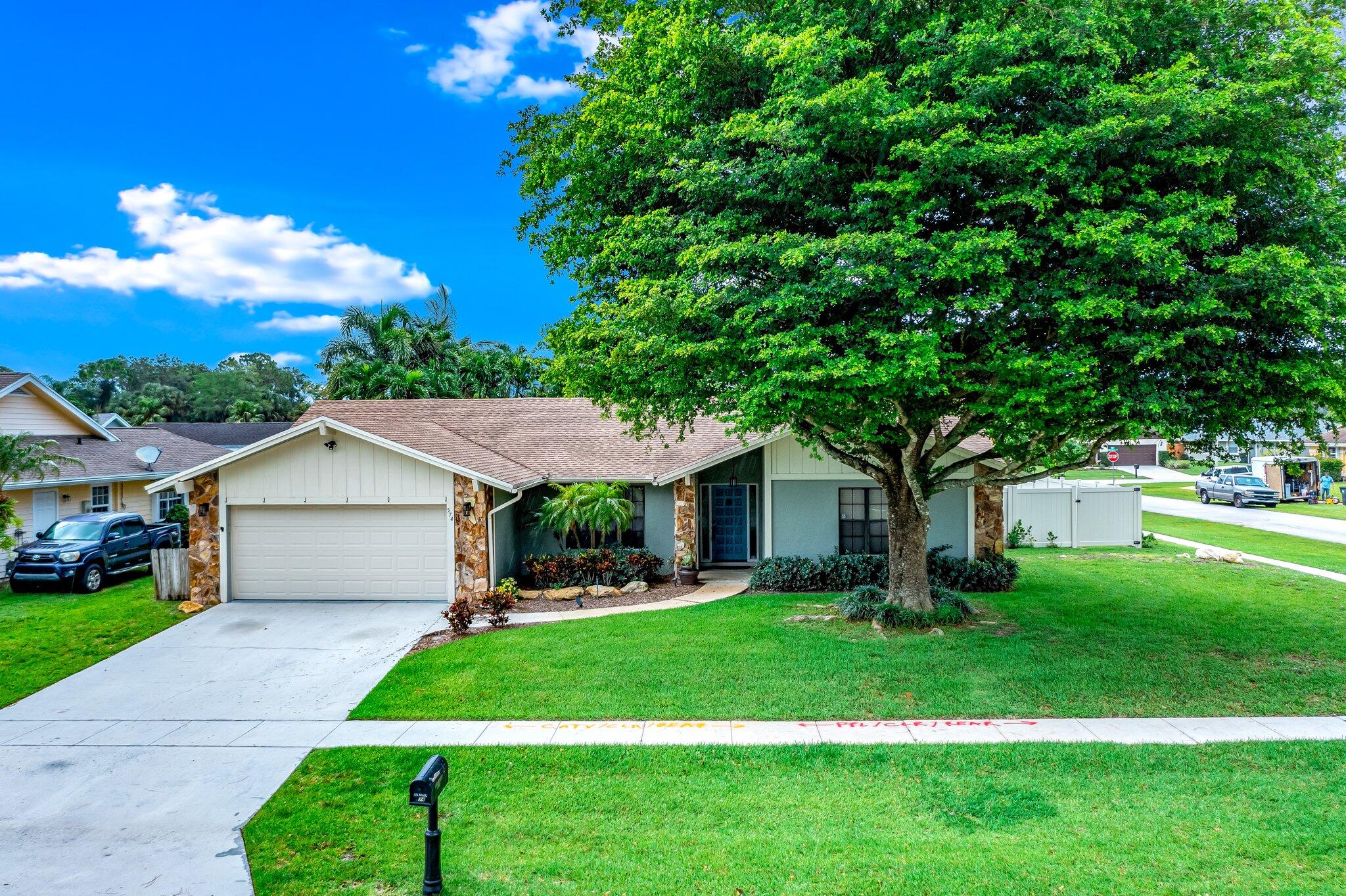 574 Juniper Place Wellington, FL 33414 - Photo 1 of 48 a front view of a house with a garden and trees