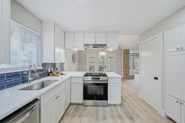 a kitchen with stainless steel appliances a stove a sink dishwasher a refrigerator white cabinets and wooden floor