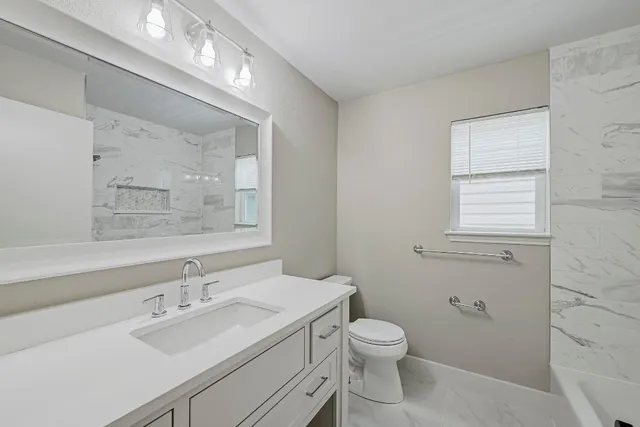 a bathroom with a toilet a sink a mirror a vanity and window