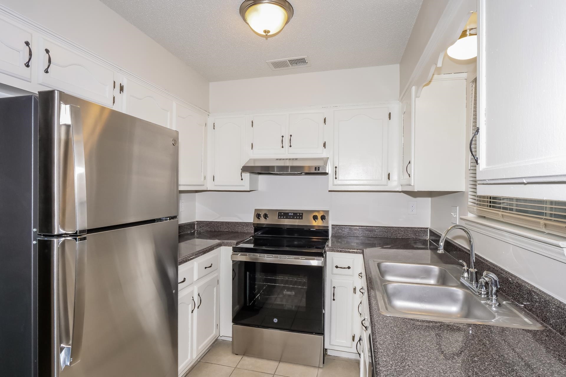 4696 Crestfield Road Millington, TN 38053 - Photo 6 of 17 Kitchen featuring appliances with stainless steel finishes, white cabinetry, under cabinet range hood, light tile patterned flooring, and a textured ceiling
