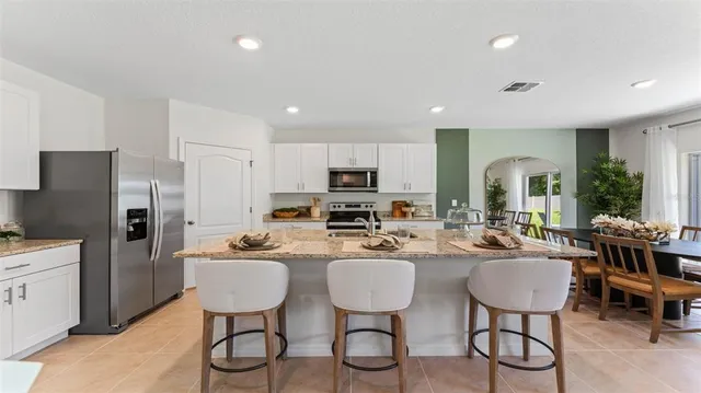 a kitchen with stainless steel appliances kitchen island granite countertop a dining table chairs refrigerator and sink
