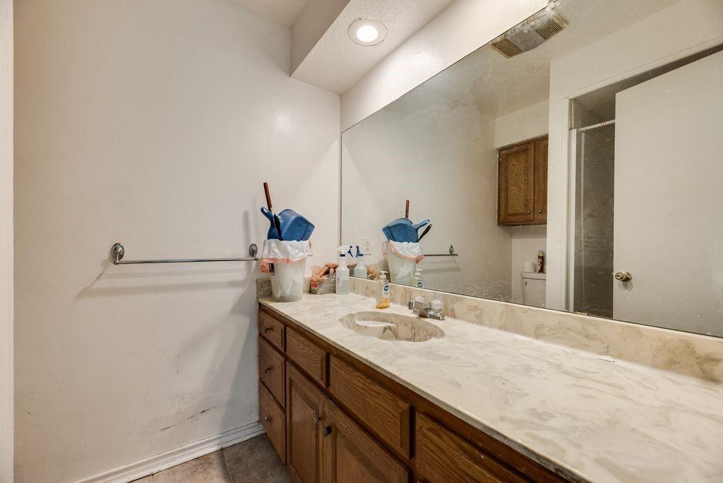 298 Butterfield Road Denison, TX 75021 - Photo 6 of 34 Bathroom vanity featuring a light-toned stone countertop, integrated sink, and wood-finish cabinetry