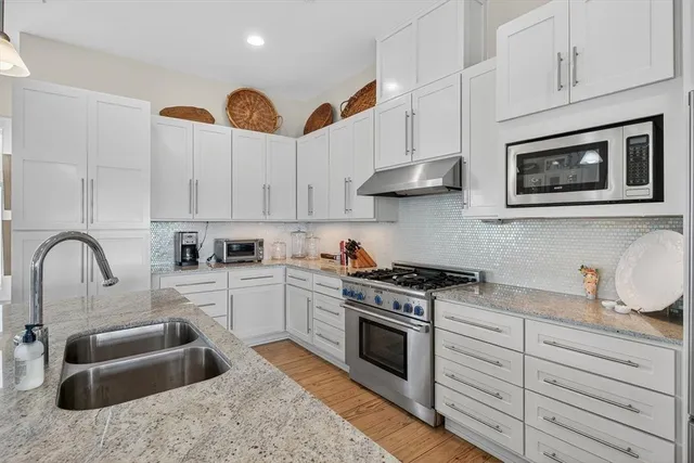 a kitchen with stainless steel appliances granite countertop a stove a sink and a white wooden cabinets