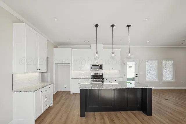 a kitchen with stainless steel appliances kitchen island granite countertop a refrigerator a stove and white cabinets with wooden floor