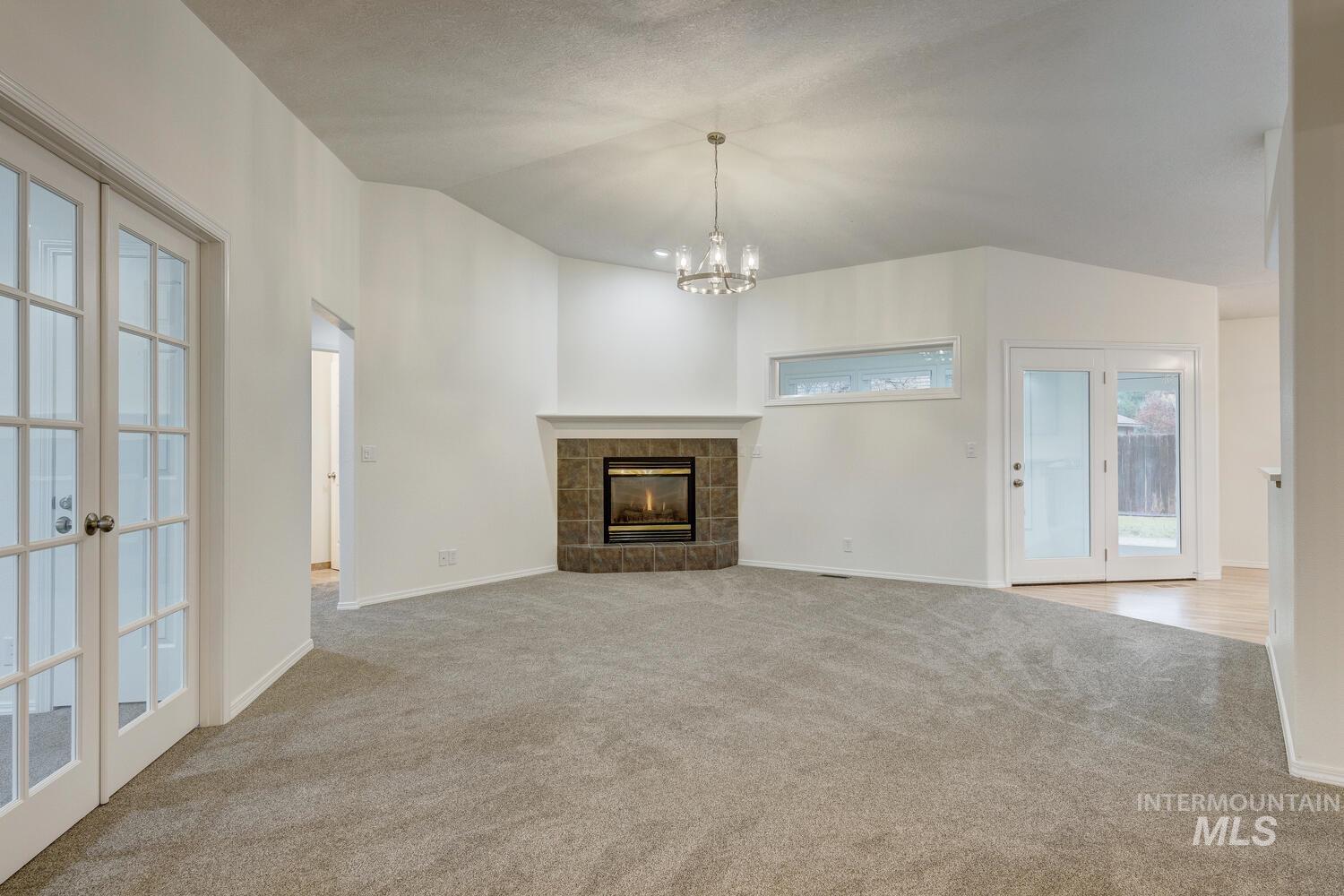 1168 North Pinnacle Way Eagle, ID 83616 - Photo 5 of 32 Unfurnished living room featuring vaulted ceiling, a tile fireplace, french doors, light colored carpet, and a chandelier
