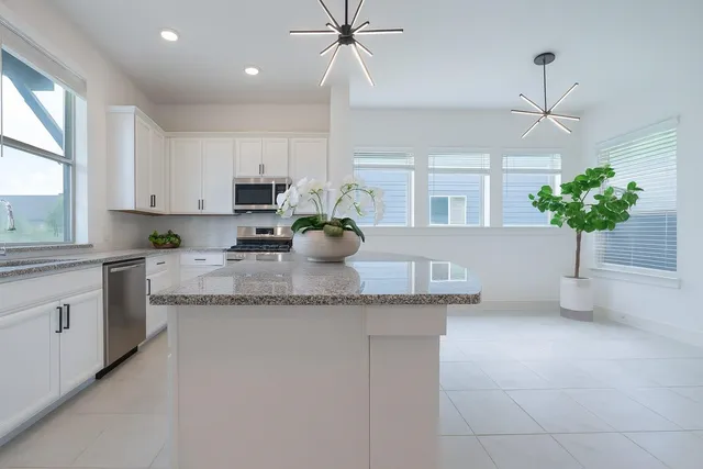 a kitchen with stainless steel appliances granite countertop a sink a window and white cabinets