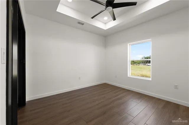 an empty room with wooden floor ceiling fan and windows
