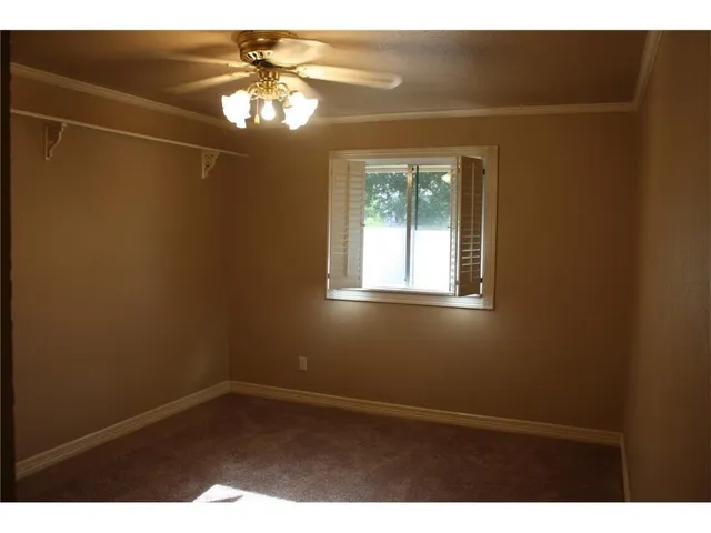 a view of an empty room with window and chandelier fan