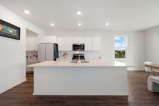 a view of kitchen with stainless steel appliances granite countertop a sink a stove a microwave a refrigerator and white cabinets with wooden floor