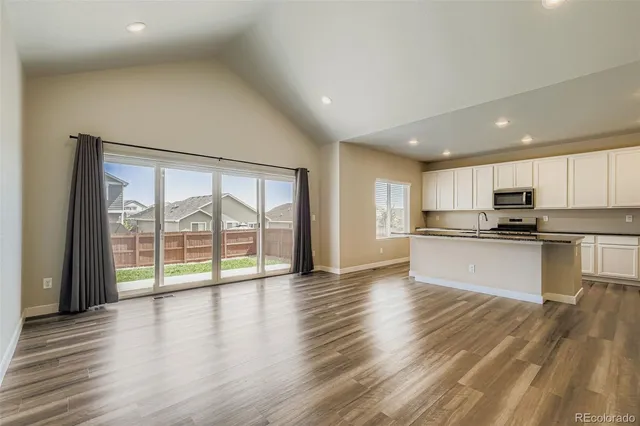 a view of an empty room with wooden floor and a kitchen