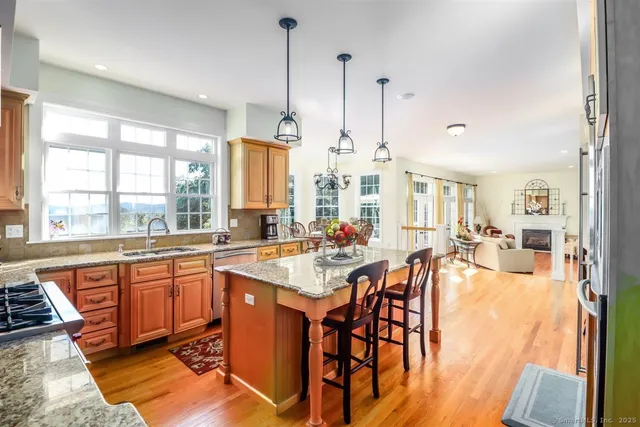 a open kitchen with stainless steel appliances granite countertop a stove top oven a sink a dining table and chairs with wooden floor