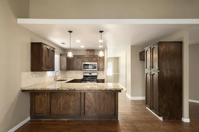 a large kitchen with granite countertop a refrigerator a sink a stove a dining table and chairs