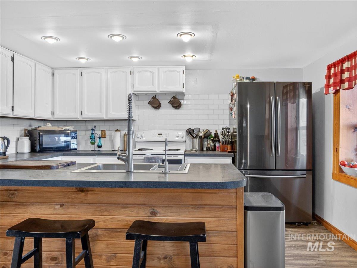 2588 West Sales Yard Road Emmett, ID 83617 - Photo 19 of 49 Kitchen with dark countertops, freestanding refrigerator, white range with electric cooktop, tasteful backsplash, and white cabinetry