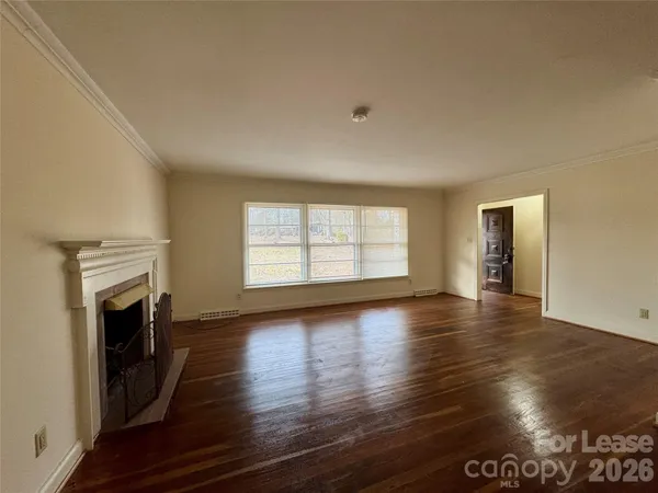 an empty room with wooden floor fireplace and windows