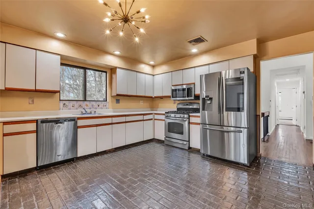a kitchen with granite countertop a refrigerator oven a sink dishwasher and white cabinets with wooden floor