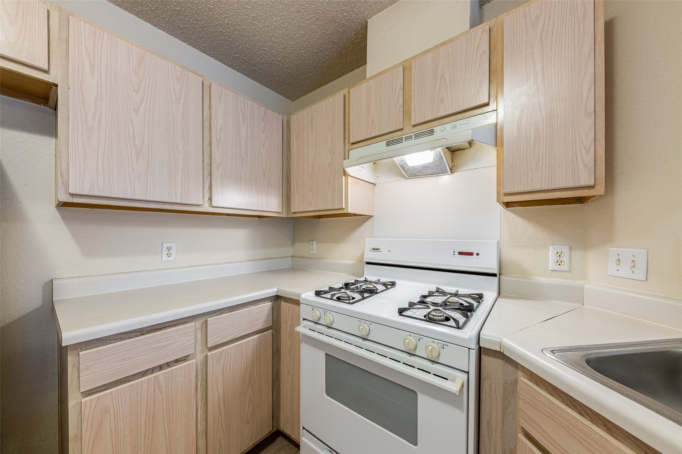 7216 Aldea Drive, Unit A Austin, TX 78745 - Photo 22 of 25 Kitchen featuring light wood-finish cabinetry, white countertops, a gas range with an overhead vent, and a stainless steel sink