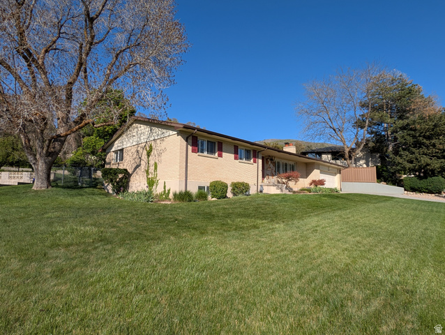 1411 Millbrook Way Bountiful, UT 84010 - Photo 2 of 36 Brick exterior with light-colored siding, a sloped front lawn, mature trees, and a concrete driveway