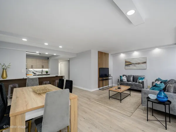 a open kitchen with stainless steel appliances kitchen island granite countertop a dining table chairs and a refrigerator