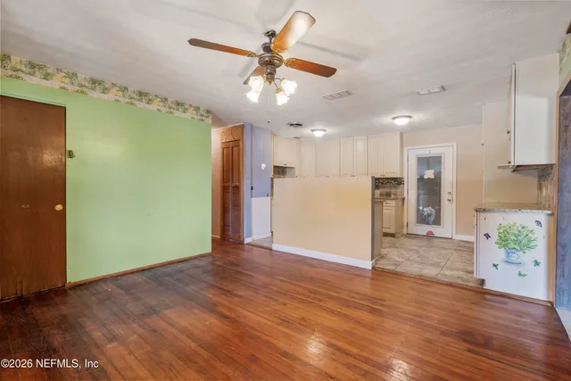 a view of an empty room with wooden floor and a kitchen