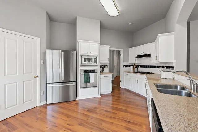 a kitchen with stainless steel appliances white cabinets a sink a stove a refrigerator and white cabinets