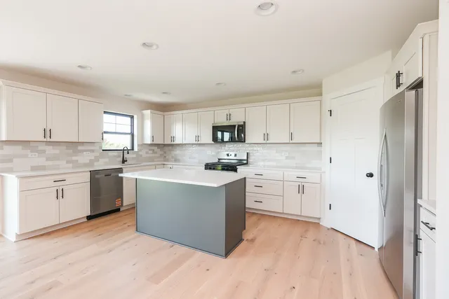 a kitchen with stainless steel appliances granite countertop a stove top oven a sink dishwasher and a refrigerator with wooden floor