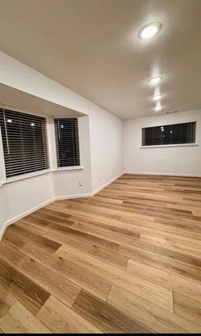 a view of an empty room with wooden floor and windows