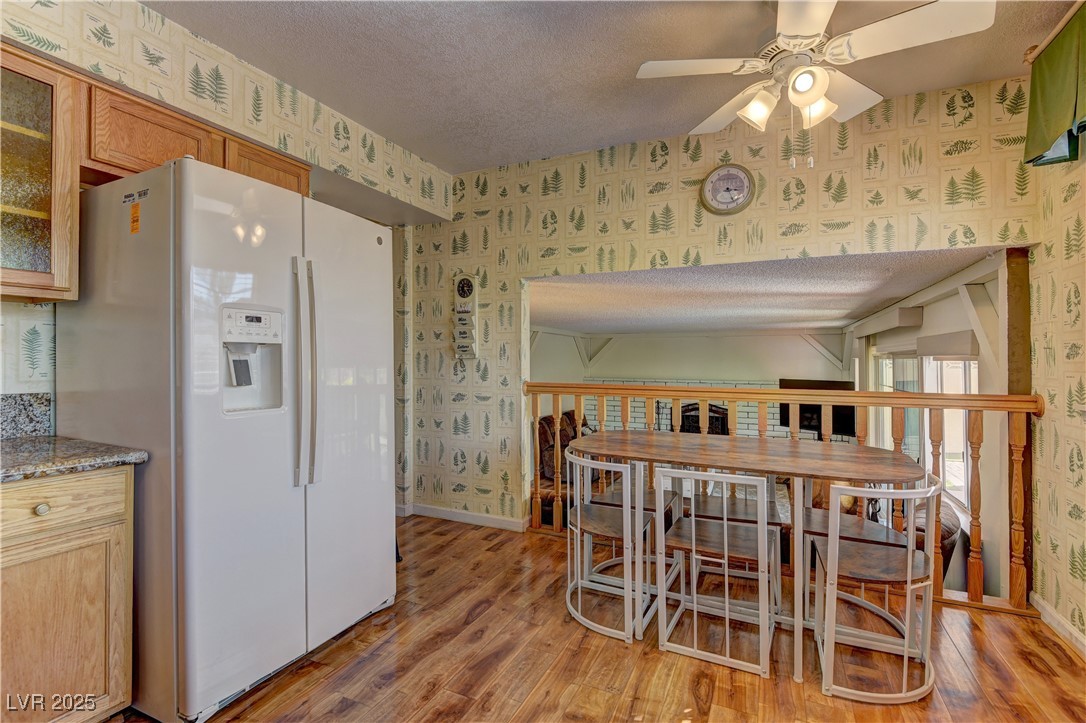 3751 El Camino Road Las Vegas, NV 89103 - Photo 12 of 27 Kitchen featuring wallpapered walls, white refrigerator with ice dispenser, glass insert cabinets, light wood-style flooring, and a textured ceiling