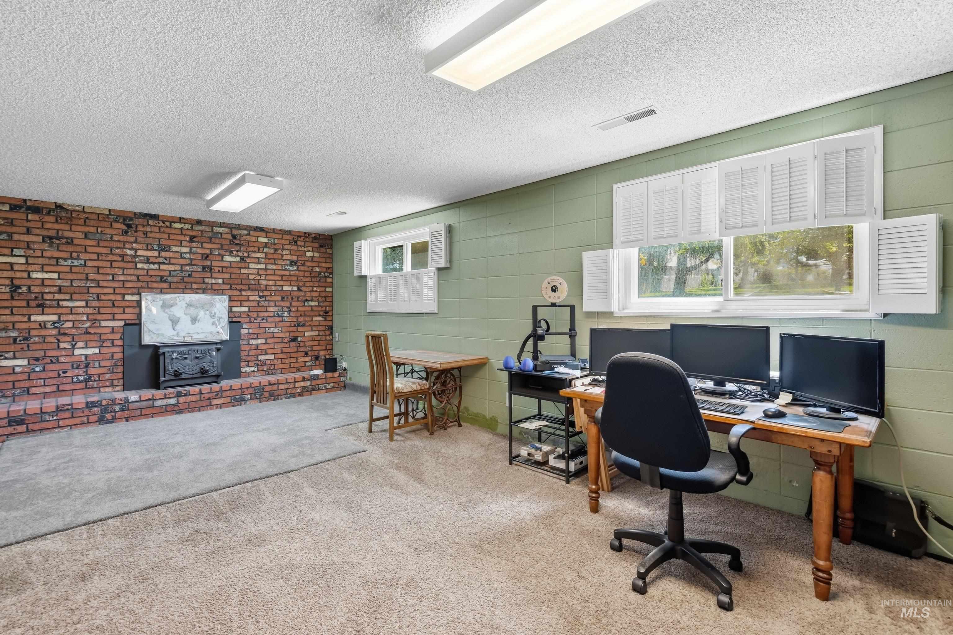 15095 David Street Caldwell, ID 83607 - Photo 18 of 39 Spacious room featuring a prominent brick fireplace with a black insert, light-colored carpeting, multiple windows with white shutters, and overhead fluorescent lighting