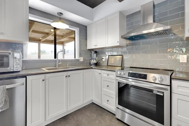 a kitchen with granite countertop white cabinets stainless steel appliances a sink and a window