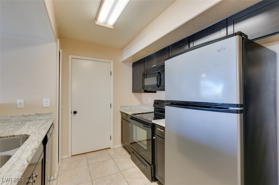 2300 East Silverado Ranch Boulevard, Unit 2190 Las Vegas, NV 89123 - Photo 28 of 41 Kitchen with black appliances, light tile patterned flooring, and light stone countertops